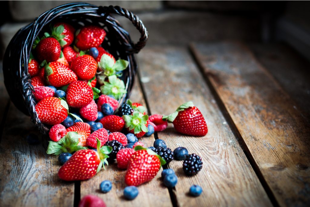 Mix of fresh berries in a basket on rustic wooden background.