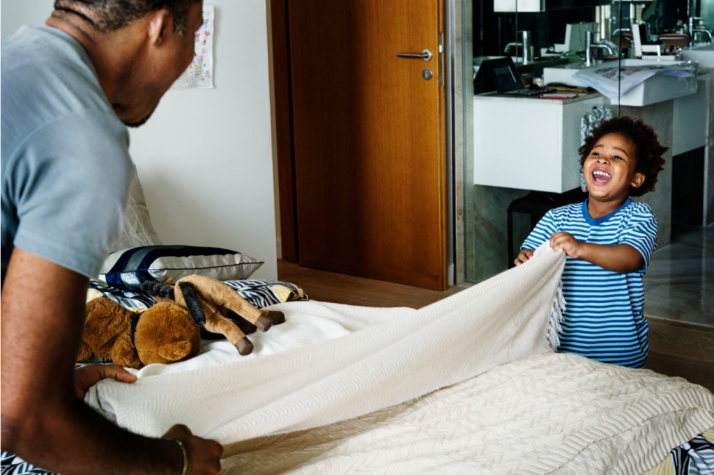 Father and son changing bedding or sheets on a bed.