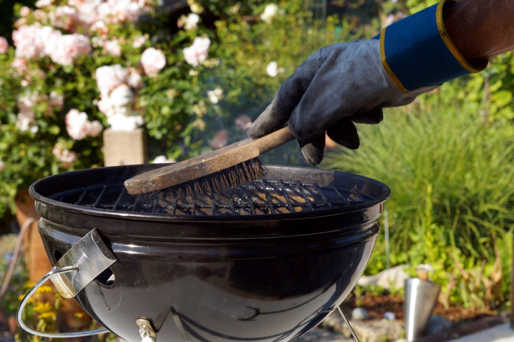 Male hand with gloves cleans round grill with stiff brush.