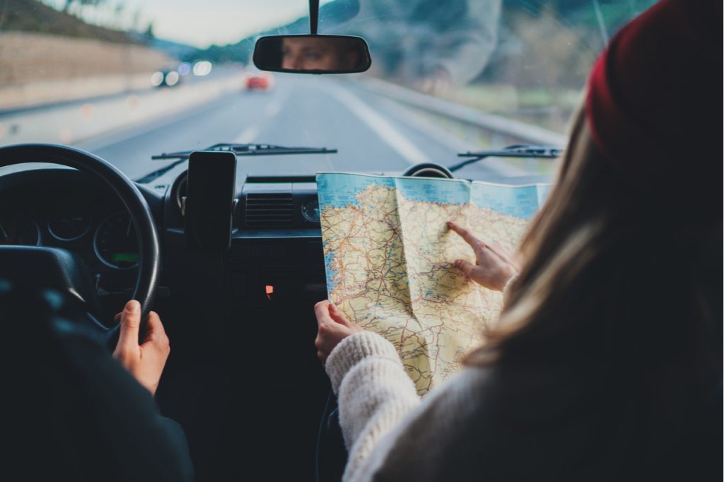 Couple in a car on a road trip, woman checking a map guiding her husband while he drives.