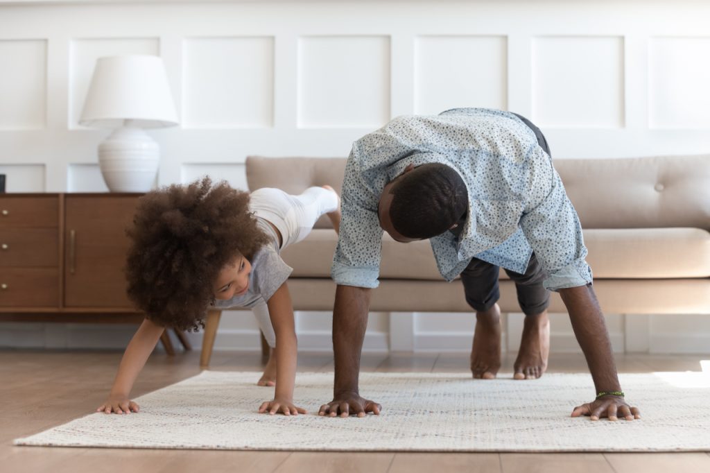 Father and daughter in casual clothes do pushup pressup exercise on carpet on warm floor in living room.