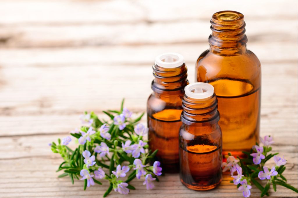 3 bottles of essential oils with small flowers on the side on a wooden surface.