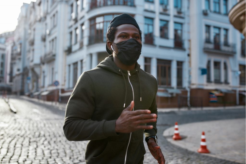 Man in black sportswear and medical protective mask running through the city street in the morning.