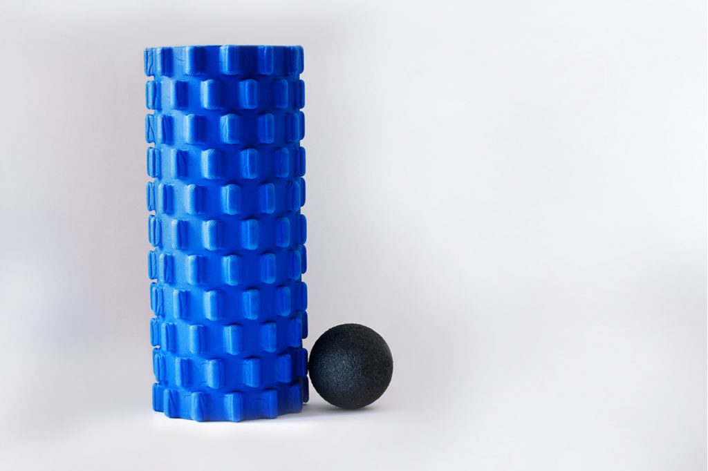 A blue foam roller right next to a black massage ball.