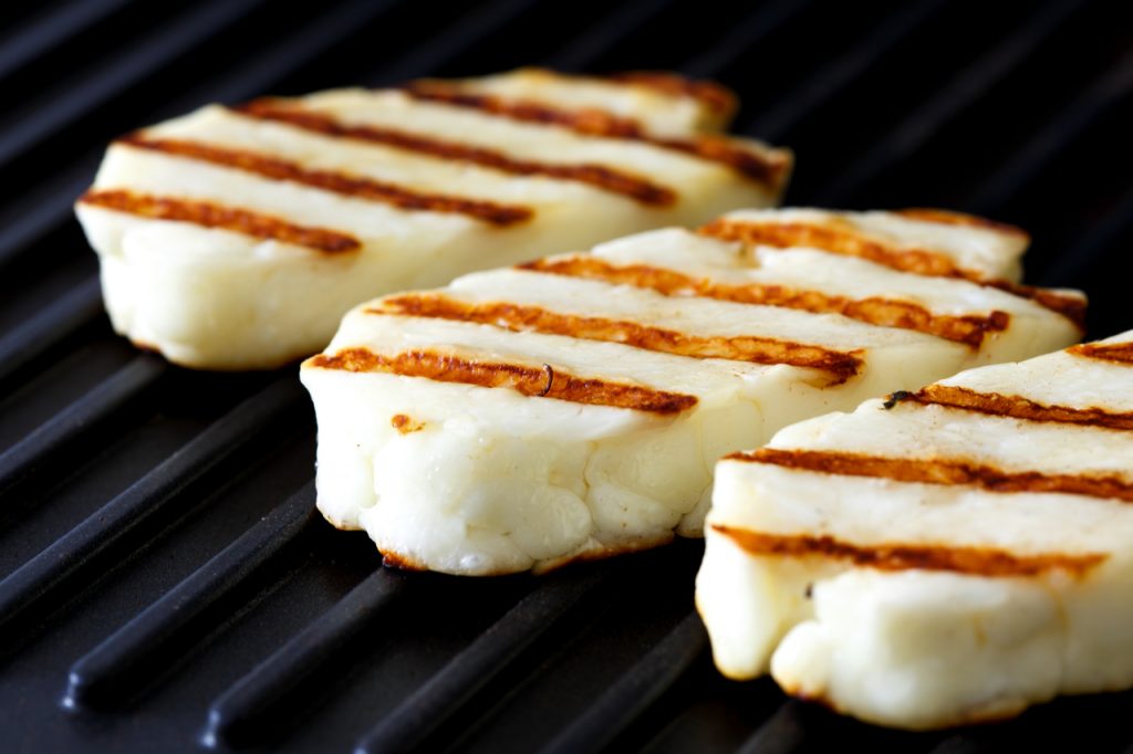 Three grilled slices of halloumi cheese on grill in perspective.