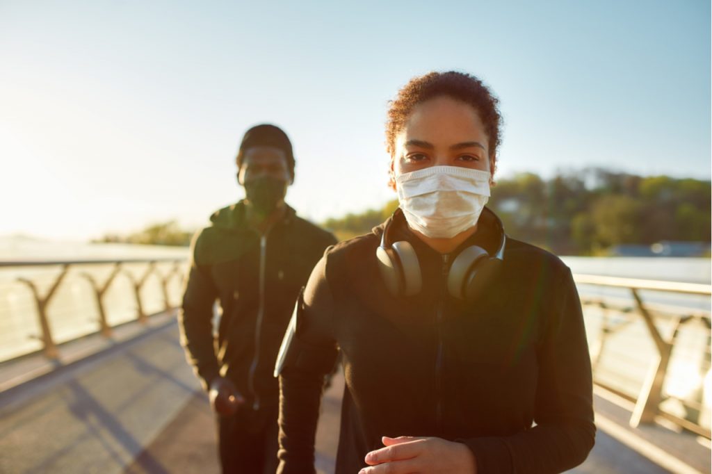 Couple wearing face medical masks while running together on the bridge in the morning.