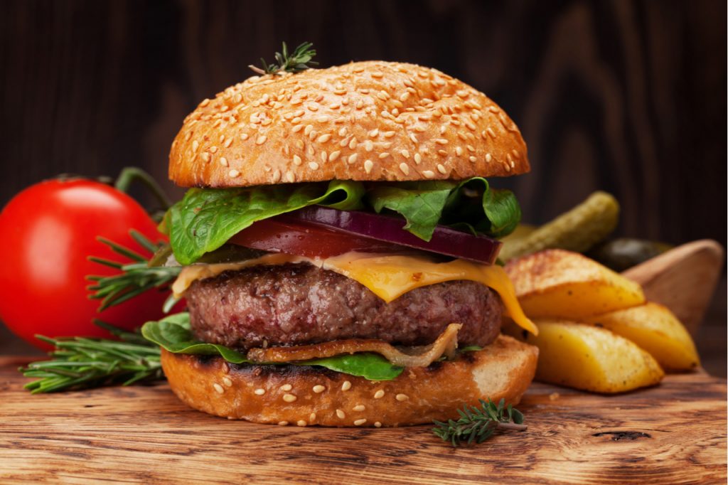 A homemade burger and a fresh tomato and potato fries on the side.