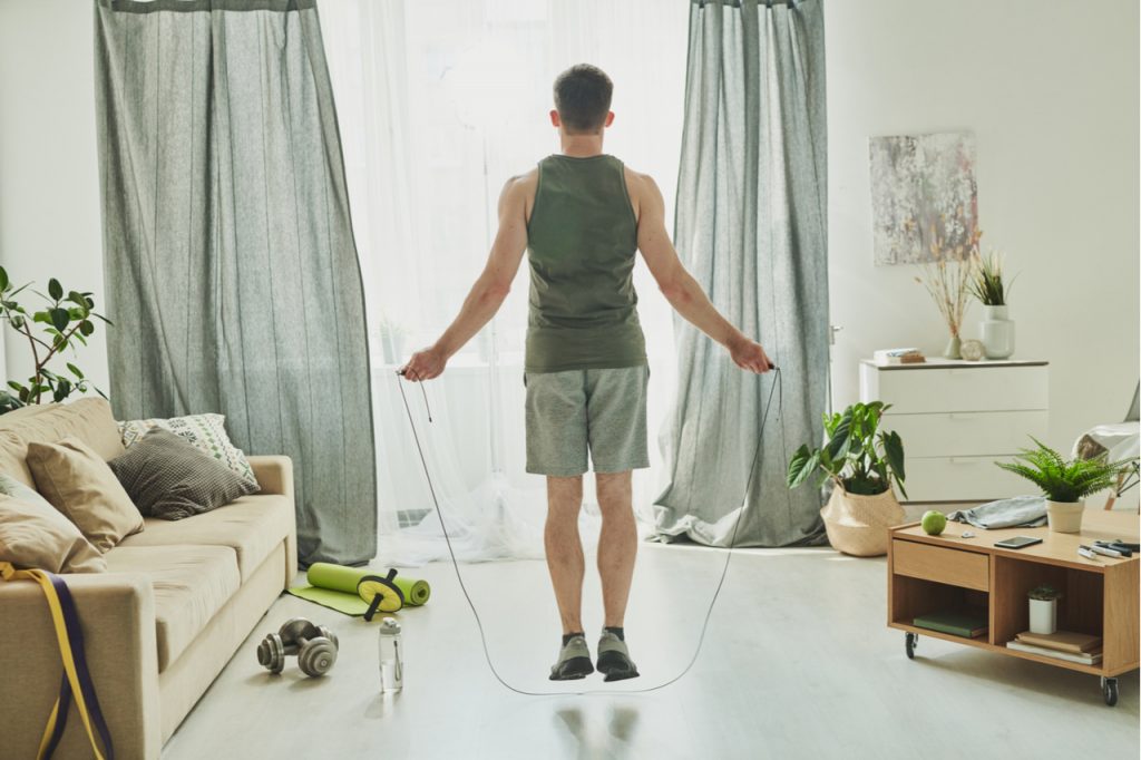 Back view of young man skipping-rope in his living room is just one of the benefits of jumping rope.