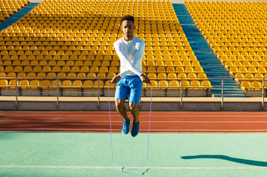 Sportsman jumping on skipping rope during workout at city stadium.