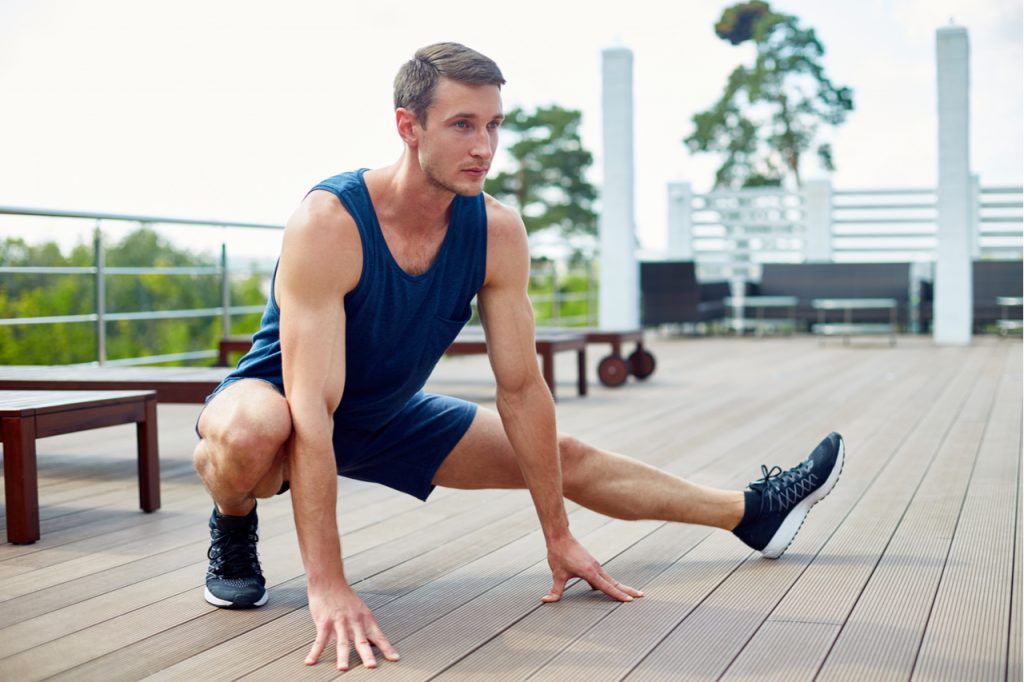 Sportsman doing side lunge while having training on spacious wooden terrace.