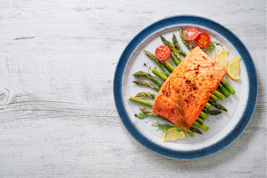Grilled salmon garnished with green asparagus and tomatoes.