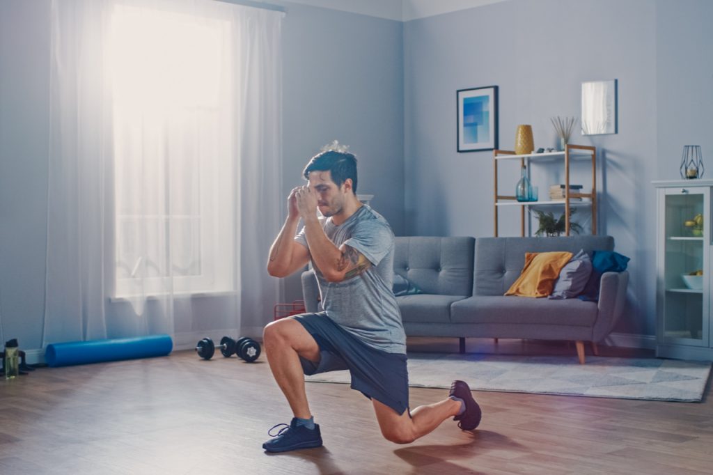 Strong athletic man doing forward lunge exercise at home.
