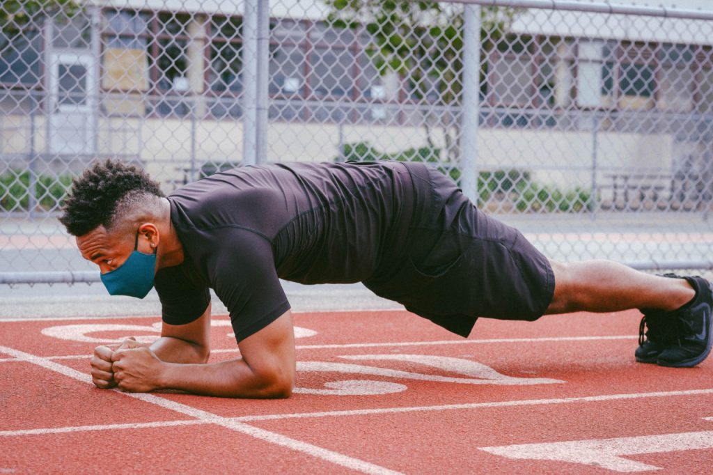 A man wearing a face mask doing planks on a running track.