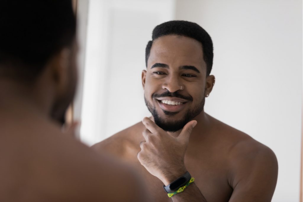 A man smiling and feeling good about himself while looking at the mirror. Positive self talk is great for the LGBTQ community.