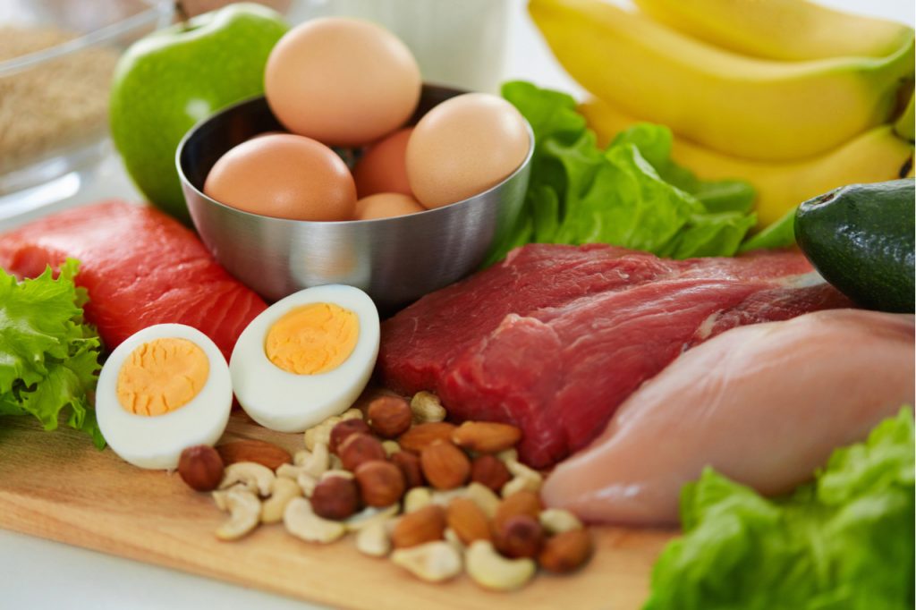 Fresh meat, salmon, hard boiled egg sliced into half, fresh eggs in a bowl, apple, bananas and nut in a wooden board are nutritious foods you need for fat loss workout.