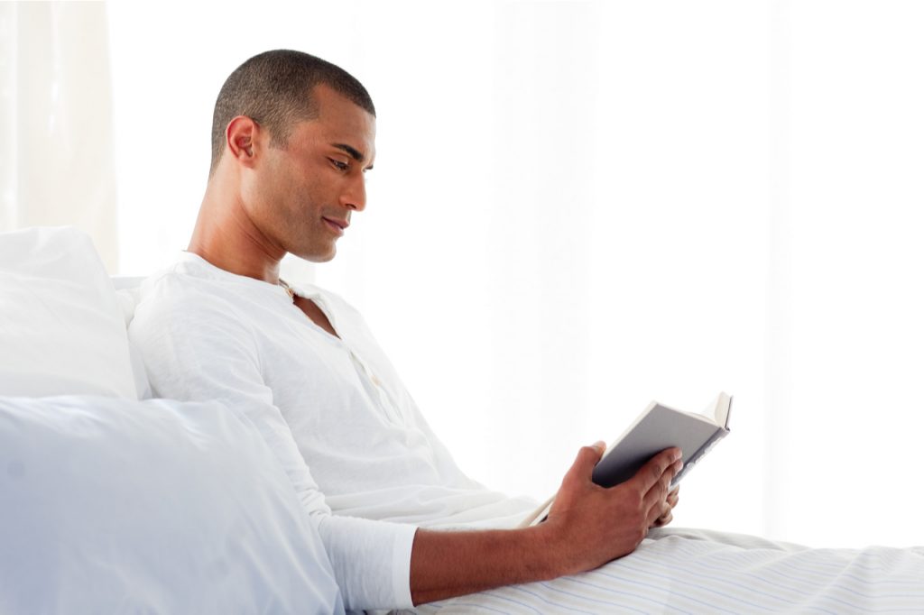 A man reading while lying on his bed.