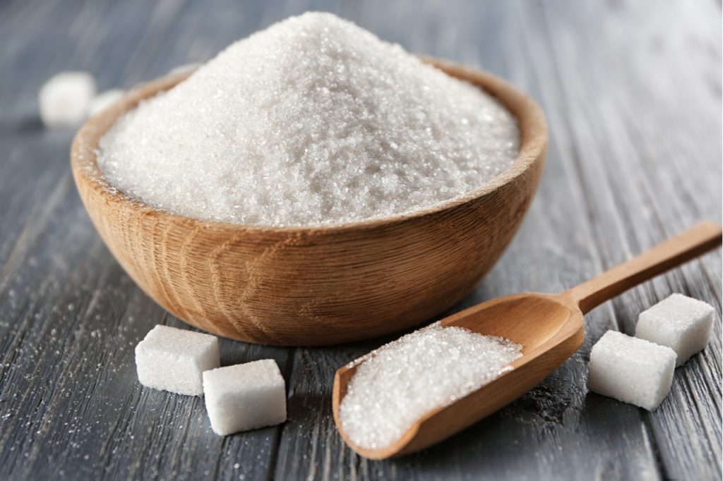 Refined sugar in a wooden bowl and on a wooden scoop and some lumps of sugar on a wooden surface. Reduce sugar intake on your diet. 