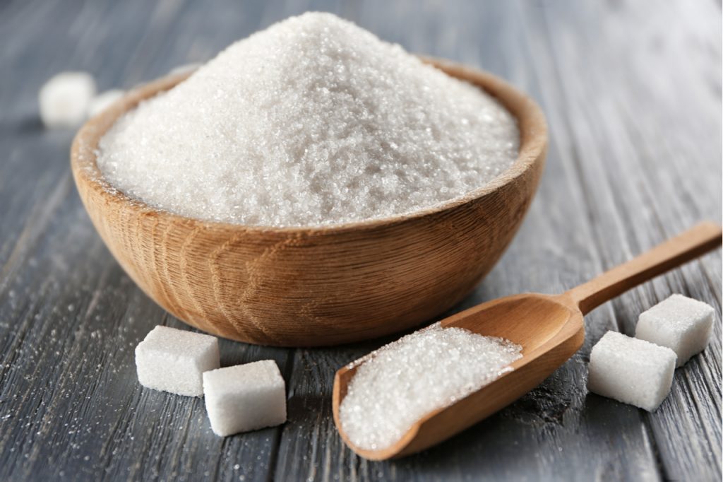 Refined sugar in a wooden bowl and on a wooden scoop and some lumps of sugar on a wooden surface. Reduce sugar intake on your diet.
