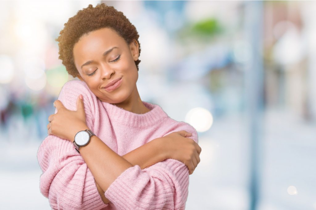 A woman hugging herself, showing self acceptance, which is one of the ways you can avoid self harm.