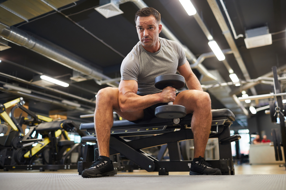man doing exercises with dumbbells during strength workout in modern gym