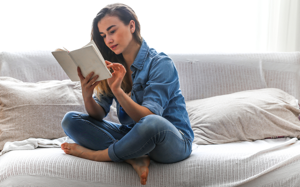 White cozy bed and a beautiful girl, reading a book, concepts of home and comfort, place for text