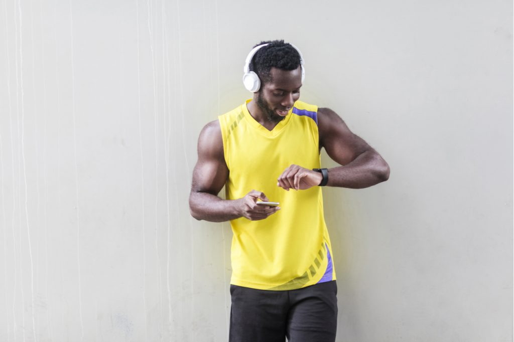 Sporty man holding smart phone and looking at smart watch.