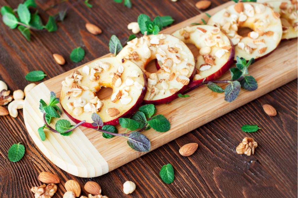 Slices of apples sprinkled with nuts and mint leaves on a wooden board.