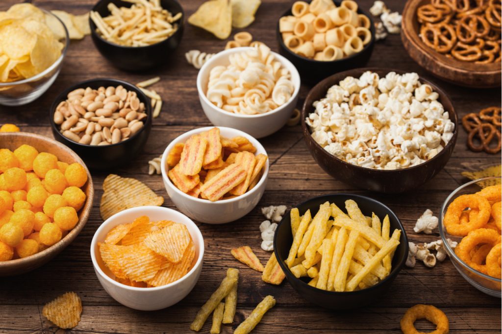 A variety of snacks in a bowl, like popcorn, nuts, pretzels, chips and fries to give you some snack ideas.