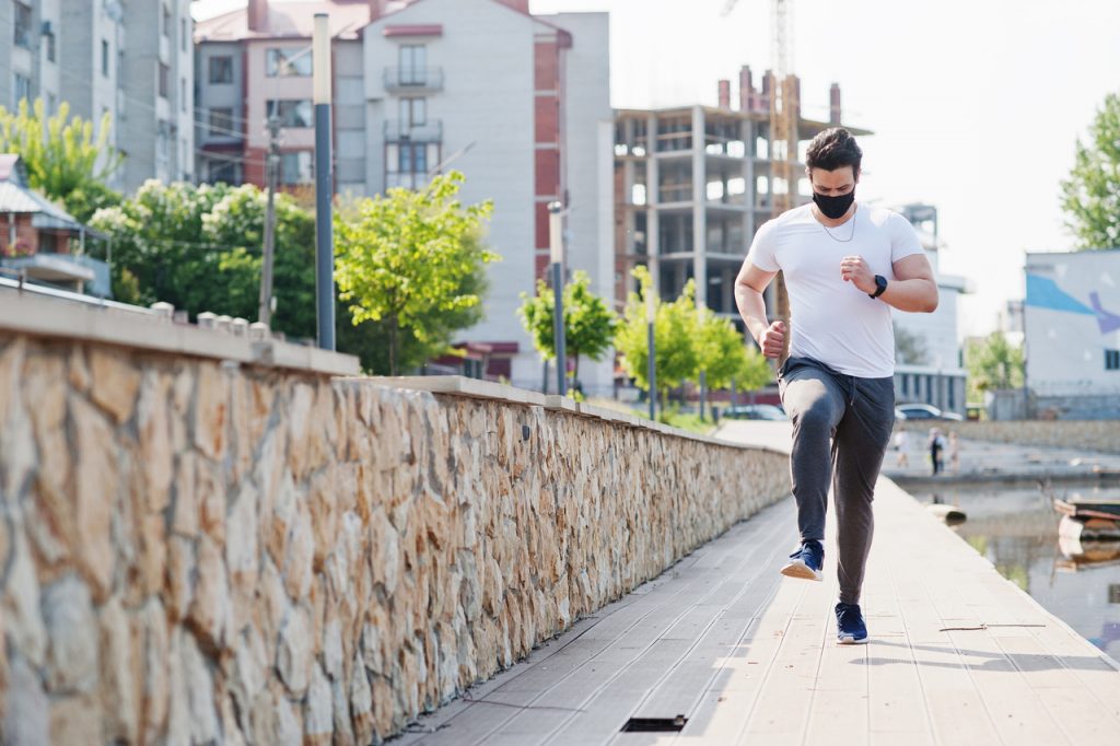 Man in black medical face mask outdoors running during pandemic coronavirus quarantine.
