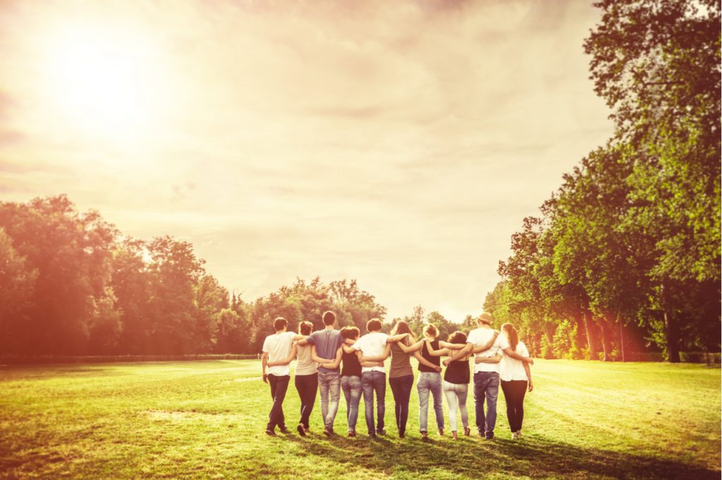 Group of friends walking on a park while holding each other.