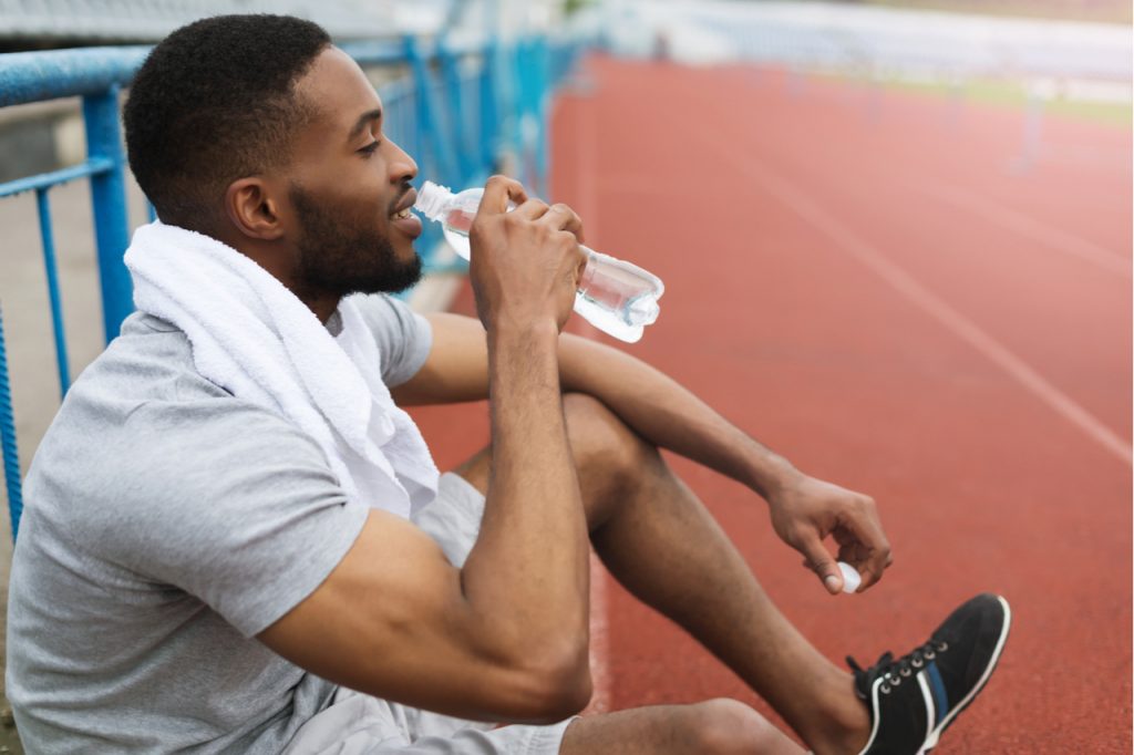 Athletic man resting after training on stadium, drinking water.