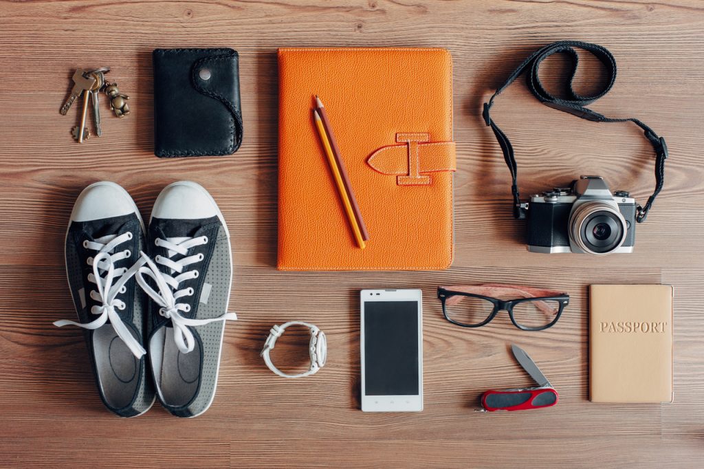 Travel essential items like a mobile phone, wallet, keys, passport, etc. on a wooden table. Make sure to follow save travel tips before and during your trip.