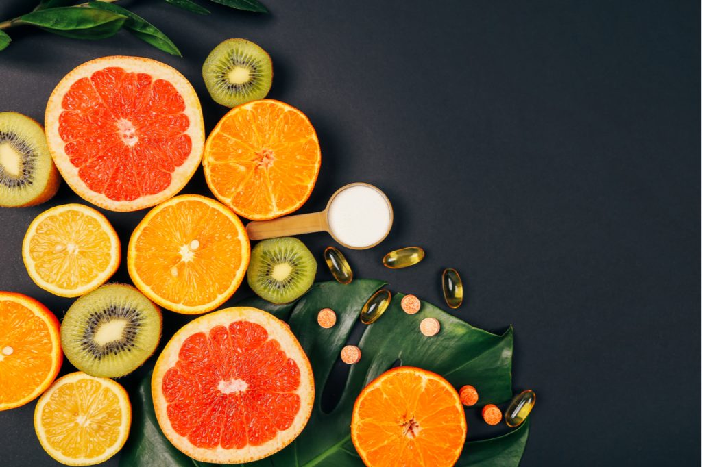Vitamins C rich fruits with vitamin c tablets and capsules on black background.