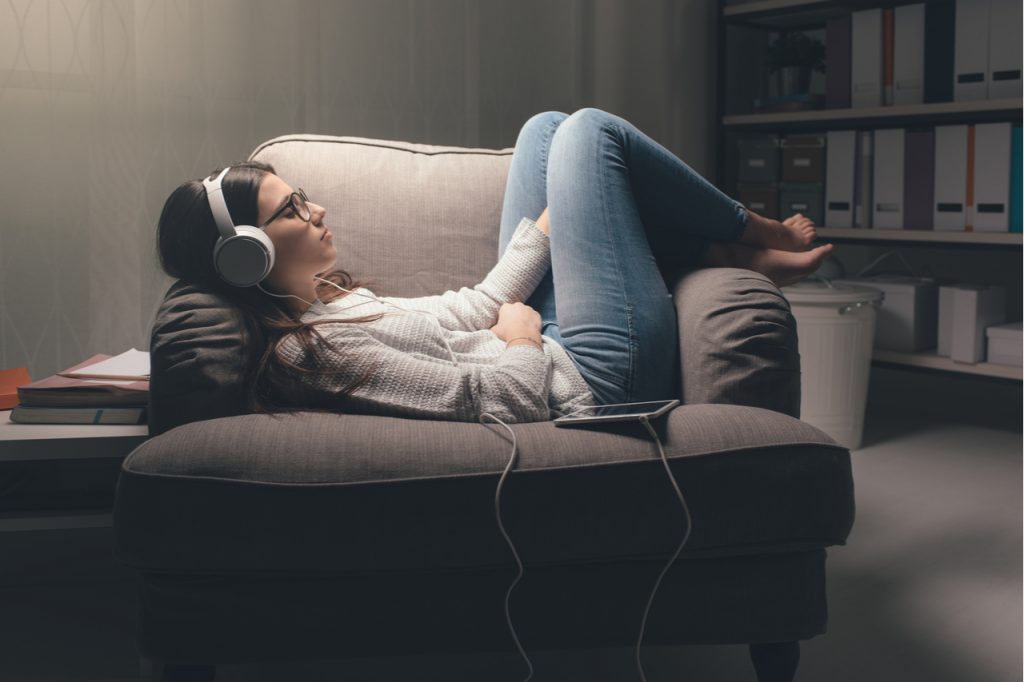 A young woman lying on an armchair with her headset on listening to music.