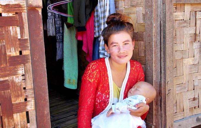 A woman sitting at the door of a hut carrying her baby.