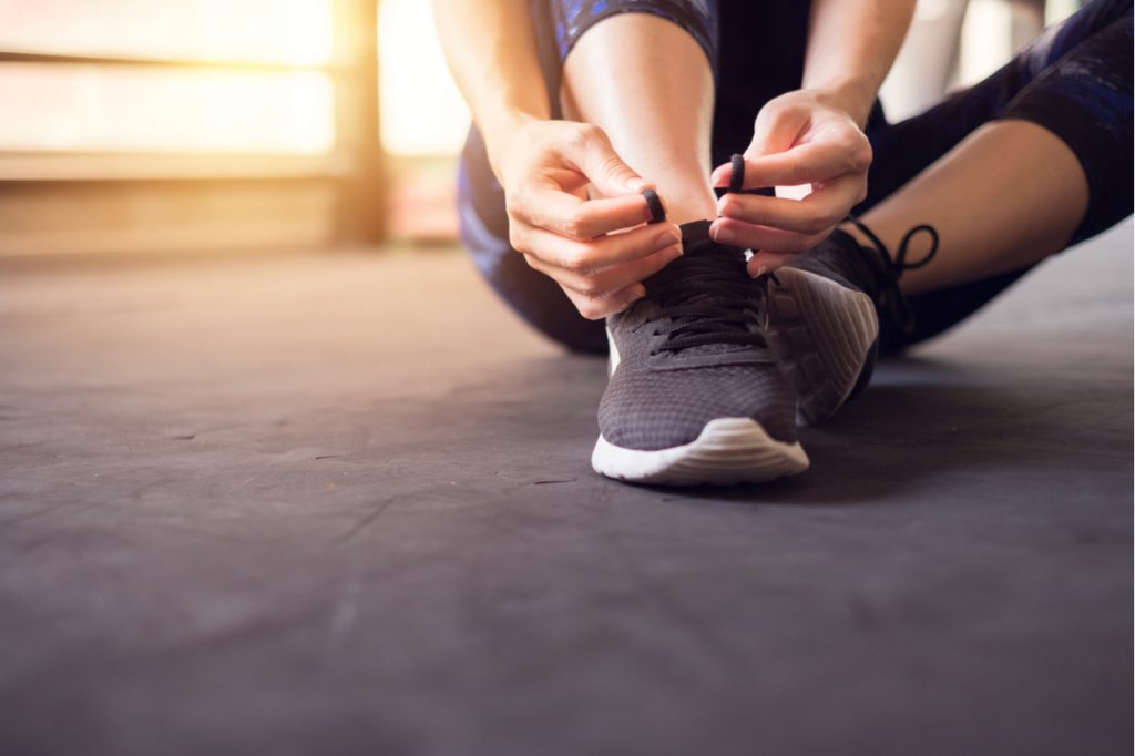 Woman tying her women's nike sneakers running shoes on black floor background in gym.