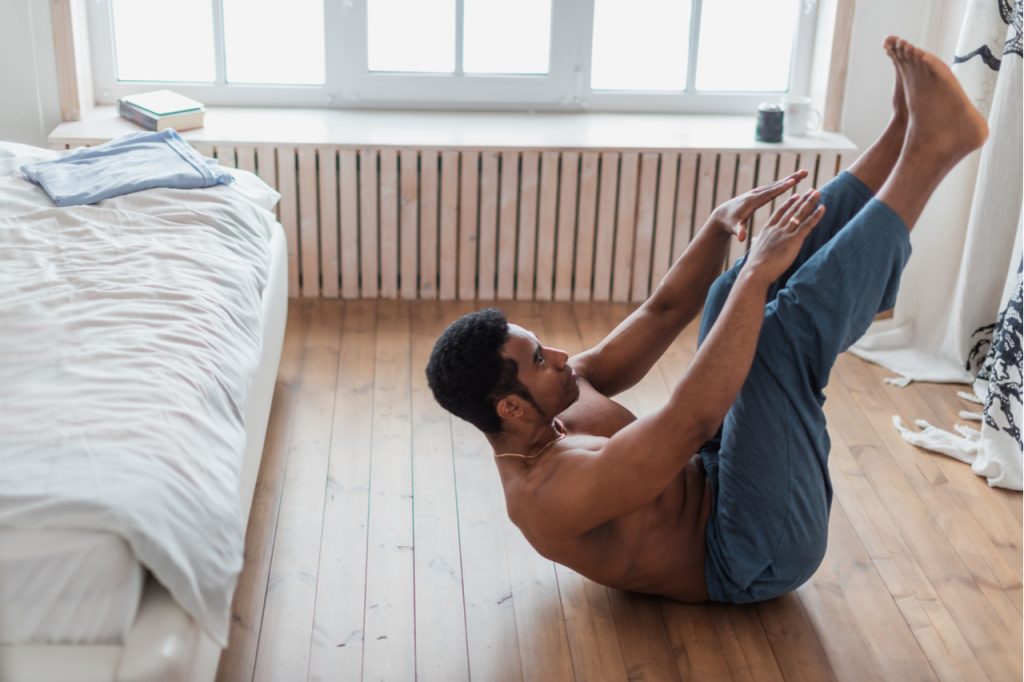 Young attractive muscular man doing morning exercise in the bedrooom.
