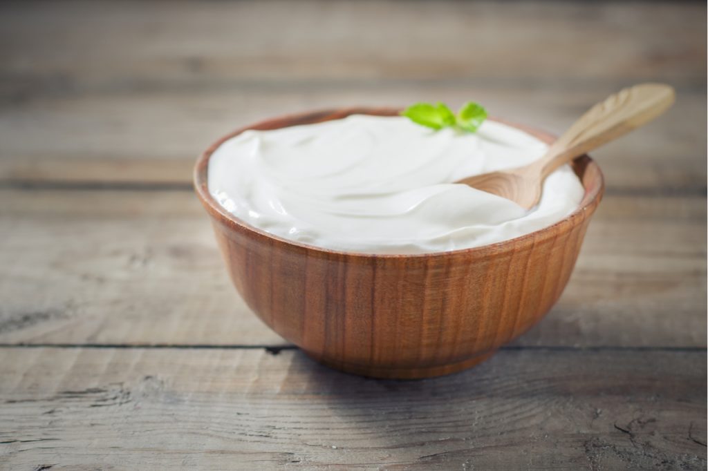 Greek yogurt in a wooden bowl on a rustic wooden table.