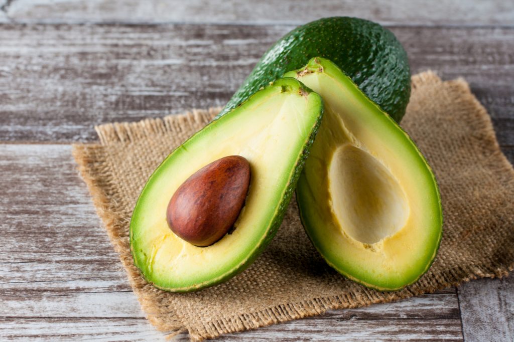 Close-up of an avocado and avocado oil on wooden table.
