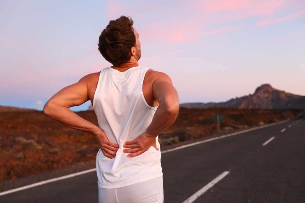 Athletic running man with neck and back pain in sportswear rubbing touching lower back muscles.