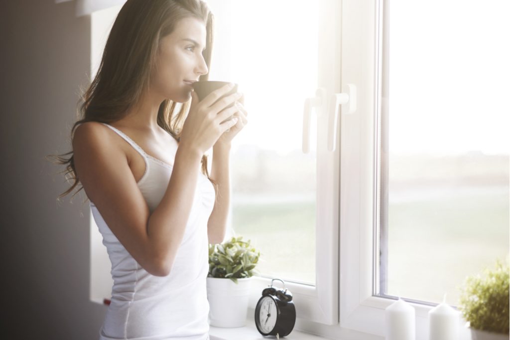 A woman drinking coffee in the morning while looking at the window.