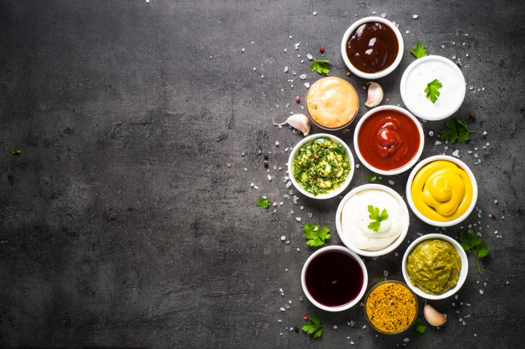 Ketchup, mayonnaise, mustard soy sauce, bbq sauce, pesto, chimichurri, mustard grains and pomegranate sauce on dark stone background.