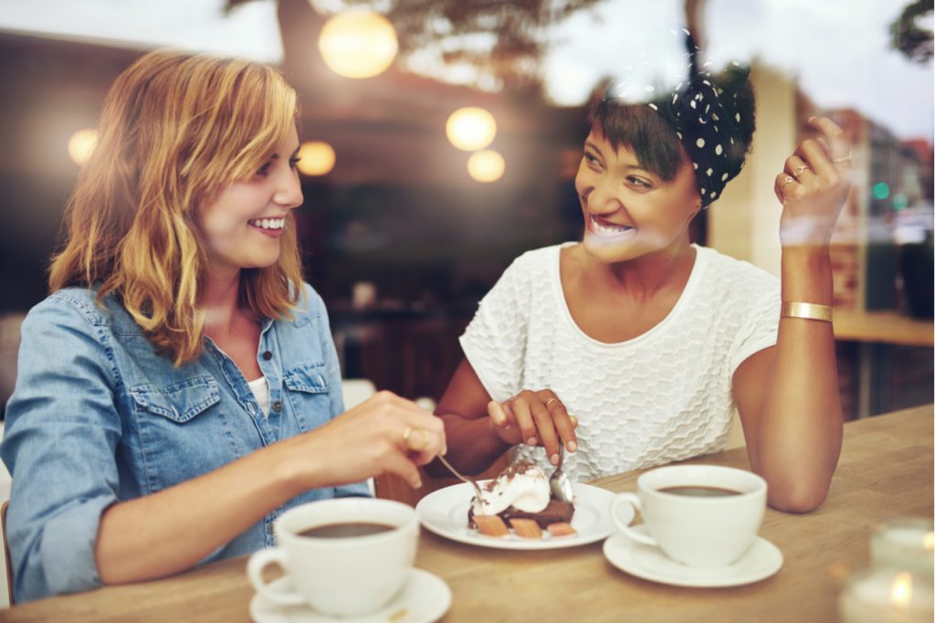Two women sharing a cake while having coffee. 
