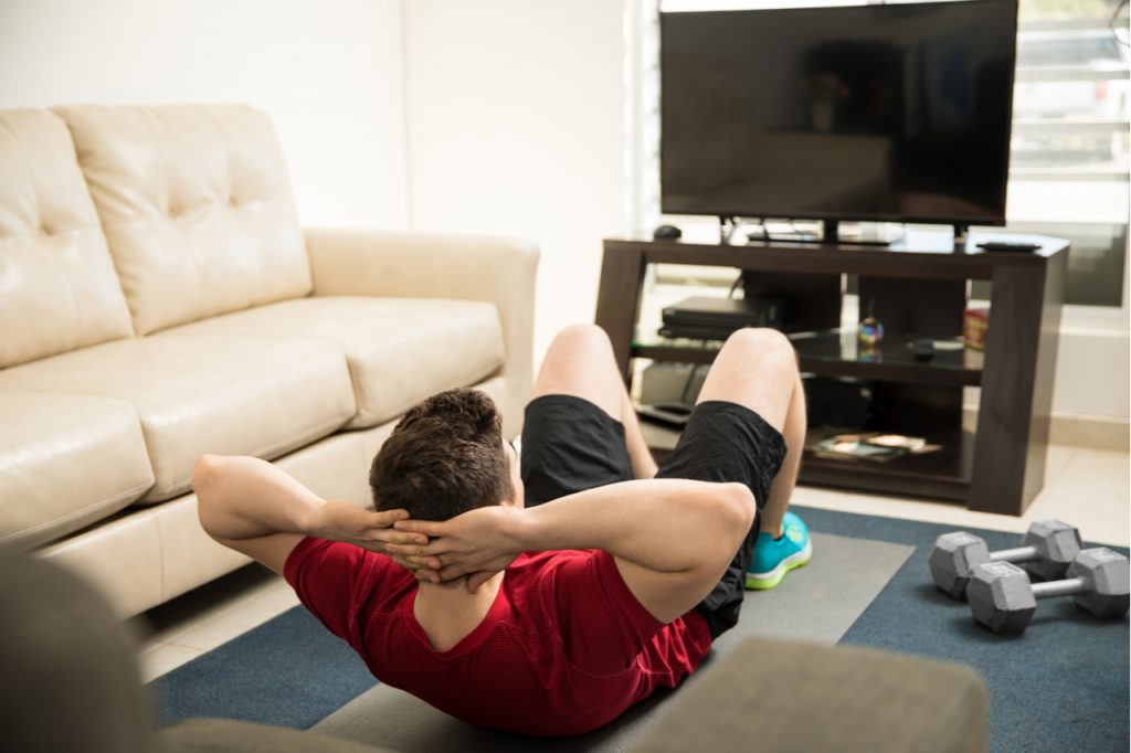 Man doing crunches in front of a television at home.