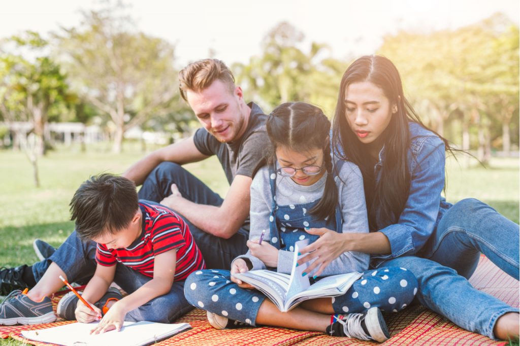 Parents helping their children with their homework while outdoors, showing a relaxed atmosphere.