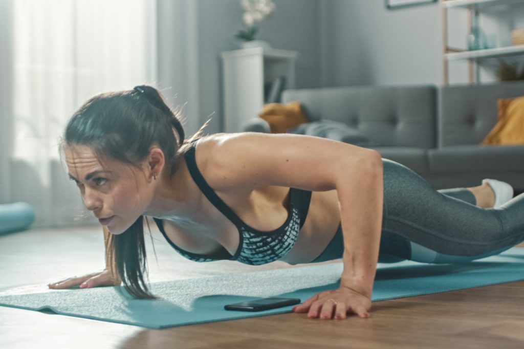 A sporty woman training at home in her living room with full body workout plan.