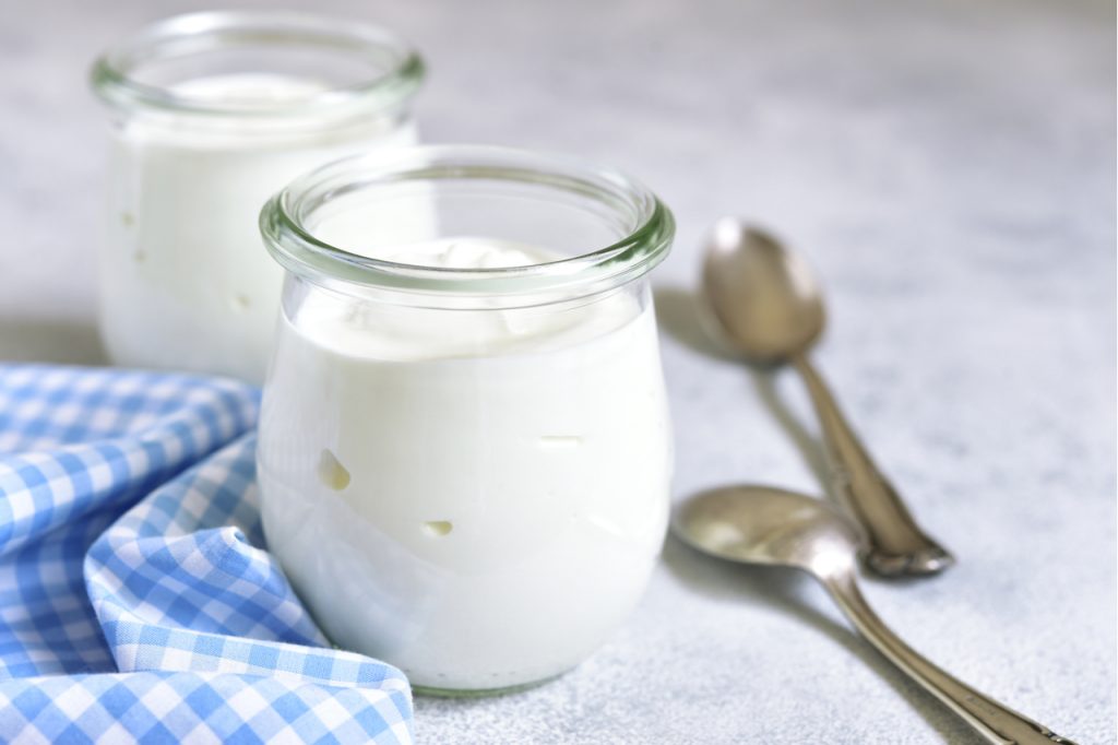Two portions of fresh natural homemade organic icelandic yogurt in a glass jar on a light slate background.