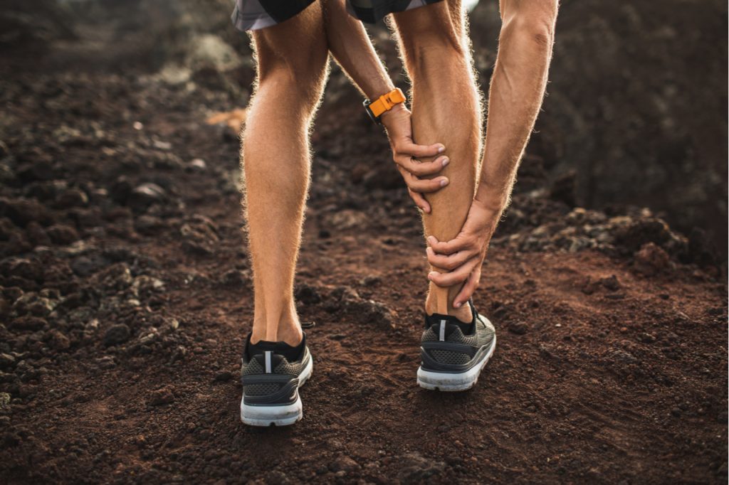 Male runner holding injured calf muscle and suffering with pain.