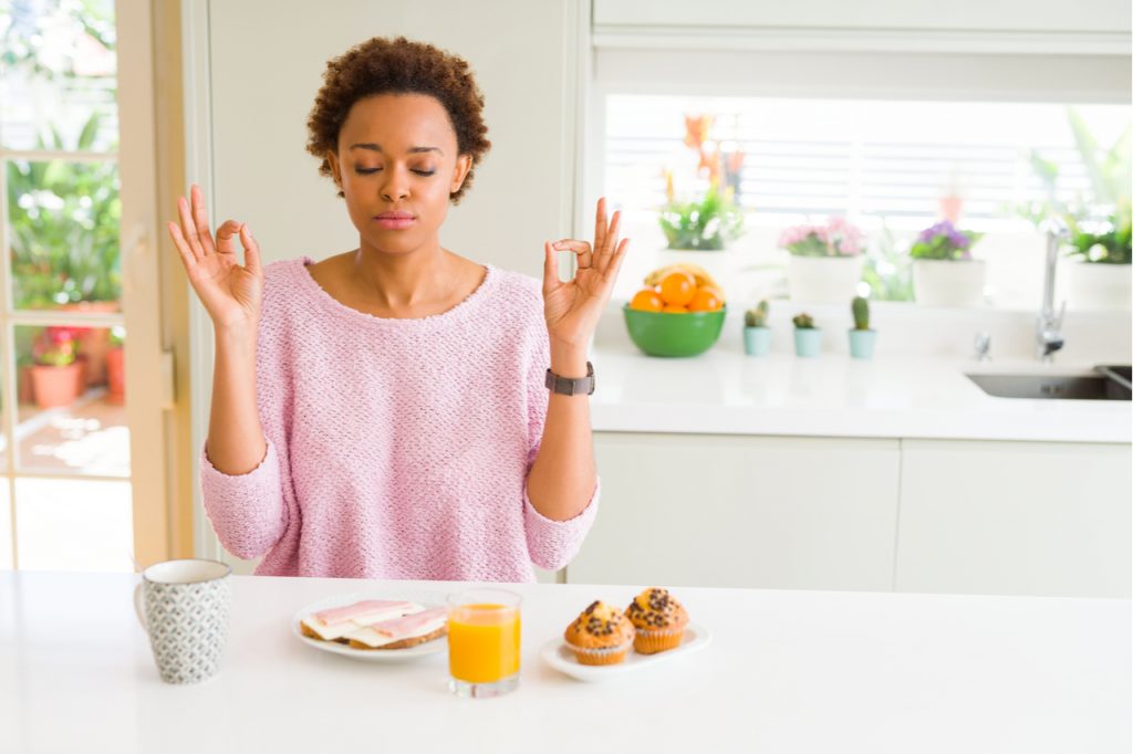 A young Afro American doing meditative eating, with food and drinks on the table. She is motivating herself on how to eat healthy.