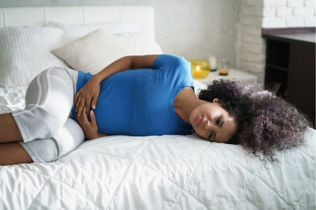 Woman having cramps during period and lying on bed at home.
